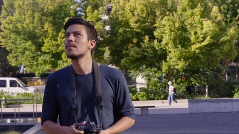 Young man walks forward while holding a camera outdoors - slow motion - shot on Stock Footage 123439644