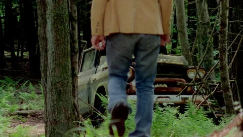 A young man walks by an old green truck in a junkyard Stock Footage 272267376