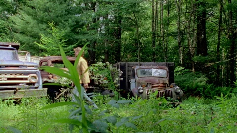 A young man walks by old trucks in a junkyard Stock Footage 272267160
