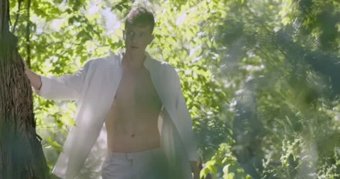 A young man walks past a tree in a green garden. Stock Footage 231544990