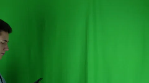 Young man walks in with phone and sideglances in front of greenscreen Vidéo 59086875