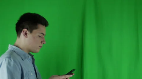 Young man walks in with phone, sideglances then leaves in front of greenscreen Vidéo 59086975
