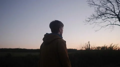 A young man walks slowly along the side of the road in the evening Stock Footage 131009727