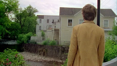 A young man walks by a stream and row of houses in on old town. Stock Footage 272251156
