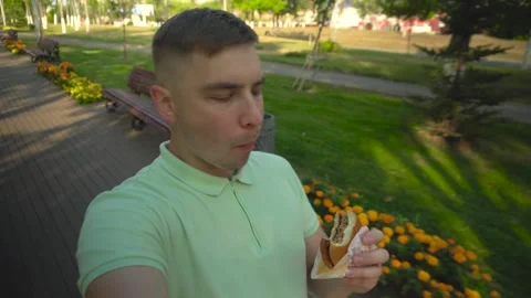 A young man walks through the park and eats a burger. A man films himself while Stock-Footage 250402112