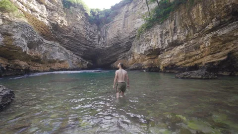 The young man walks through the water in the seaside cave with a fascinating vie Video stock 212490964