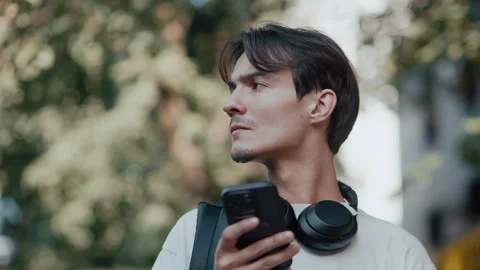 Young man walks in urban setting listening to music on smartphone Stock Footage 339215778