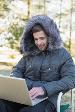 Young man in warm clothing using laptop in the forest Stock Photos