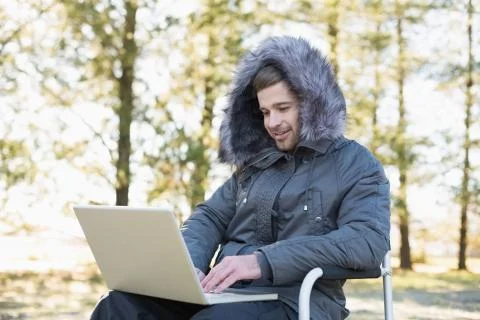 Young man in warm clothing using laptop in the forest Stock Photos