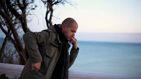 A young man in a warm jacket lights a cigarette Against the background of the se Stock Footage 150226934