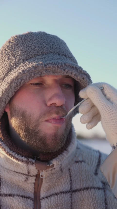 Young man in warm outfit eats red velvet cake from girlfriend hand on winter day Video stock 329291434