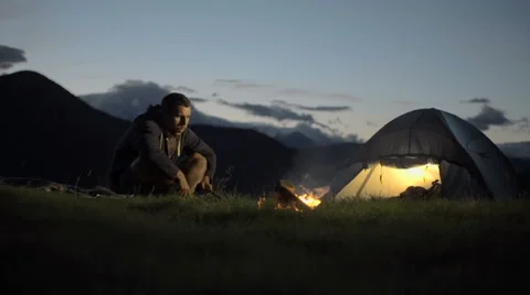 Young man warming with camp fire in nature mountain outdoor camping scene 動画素材 64543627