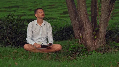 The young man was sitting on the grass under a tree and enjoying the peace and Stock Footage 115030414