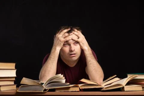 A young man was sitting at a table above books, holding his head in his hands. Stock Photos