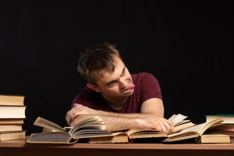 A young man was sitting at a table above books, holding his head in his hands Foto stock