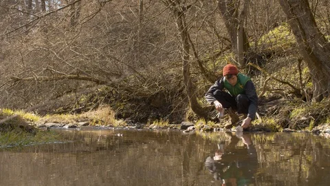 Young man washes the dishes in a forest river Stock Footage 129077654