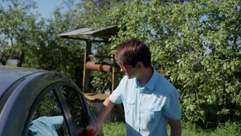 A young man washes his car with a rag near the house on a sunny day. Stock Footage 136028792