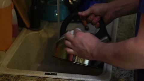Young man washes the kettle with detergent in the kitchen sink, hands close up Stock Footage 112684484