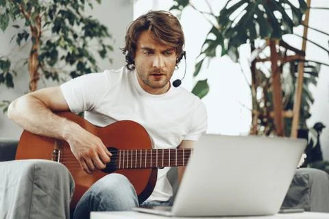 Young man watching guitar tutorial on his laptop Stock Photos