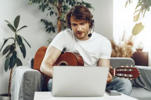 Young man watching guitar tutorial on his laptop 写真素材