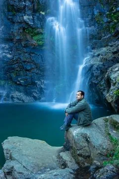 Young man at waterfall falling from mountain with calm blurred water surface  Foto stock