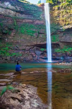Young man at waterfall falling streams from mountain top with reflection from 写真素材