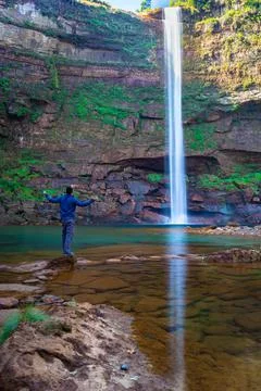 Young man at waterfall falling streams from mountain top with reflection from 스톡 사진