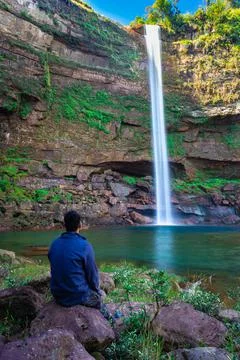 Young man at waterfall falling streams from mountain top with reflection from Фото