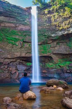 Young man at waterfall falling streams from mountain top with reflection from Stock-Fotos