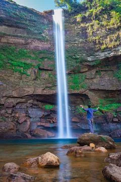 Young man at waterfall falling streams from mountain top with reflection from Stock-Fotos
