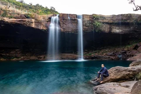 Young man with waterfall streams falling from mountain top at morning long ex 写真素材