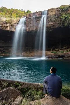 Young man with waterfall streams falling from mountain top at morning long ex 写真素材