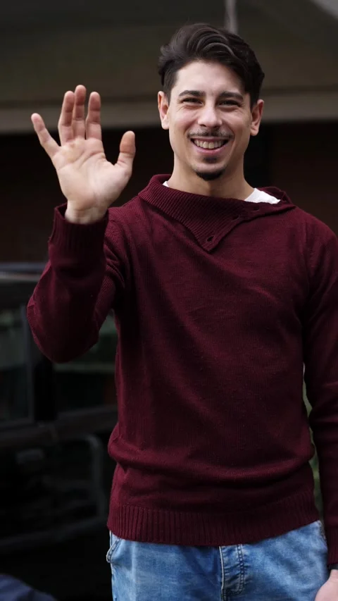 Young man waves gently at the camera with a soft, friendly smile Stock Footage 306678158
