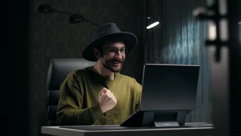 Young man wear hat celebration victory using laptop in dark room.Beard guy with Stock Footage 232134599