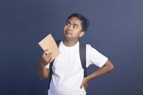 Young man wearing a backpack and holding a notebook while looking up with a.. Stock Photos