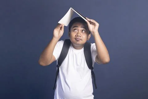 Young man wearing a backpack holding an open notebook over his head like a .. Stock Photos