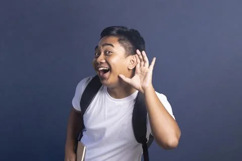 Young man wearing a backpack holding a hand to his ear as if listening or e.. Stock Photos