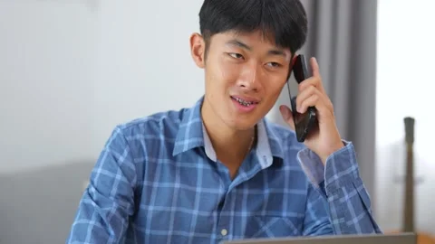 Young man wearing blue checkered shirt talking on smartphone while sitting .. Stock Footage 332979702