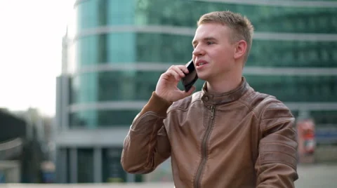 Young man wearing a leather jacket talks on the phone in downtown slow motion Stock Footage 62326352
