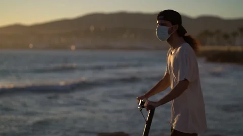 Young man wearing mask uses electric scooter on sunset near sea Video stock 147833765