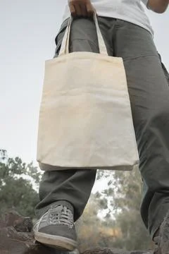 Young man wearing a plain white t-shirt holding a clean white tote bag. Cle.. Stock Photos