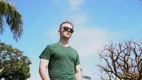 Young man wearing sunglasses stands against a blue sky Stock Footage 153977053