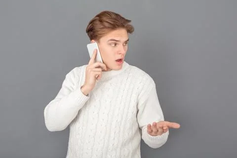 Young man wearing sweater studio isolated on grey talking using smartphone Foto stock