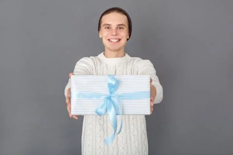 Young man wearing sweater studio isolated on grey giving present close-up Stock Photos