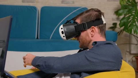Young man wearing virtual reality headset, play at the laptop. Augmented Reality Stock Footage 141264231