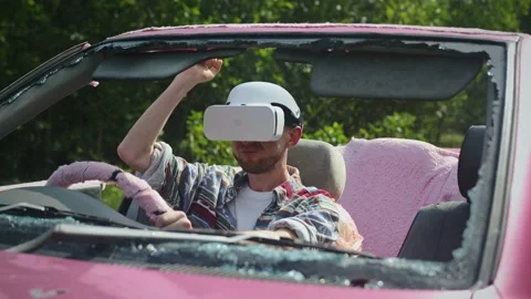 Young man wearing virtual reality goggles sits in broken car and uses horn Stock Footage 237166230
