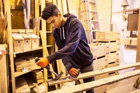 Young man wearing work gloves standing in warehouse, removing rusty nails from Stock Photos