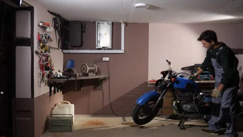 Young man wearing work overalls and gloves repairing a vintage blue motorcycle Stock Footage 342773829