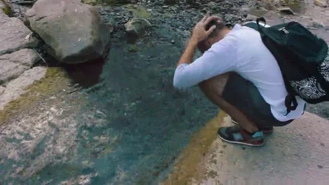 Young man wets his head in a clean, cool mountain stream. Video stock 69184584