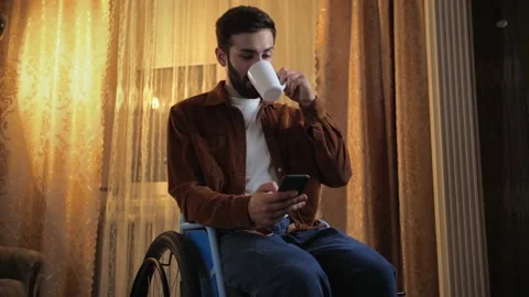Young man in a wheelchair drinks tea and uses his phone for online shopping. Stock Footage 202116531